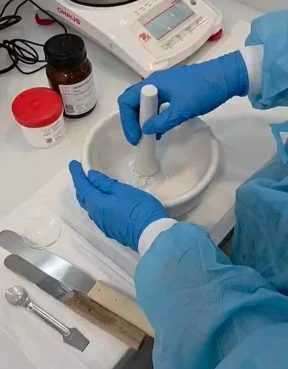 Preparação de uma fórmula num almofariz com mãos protegidas por luvas